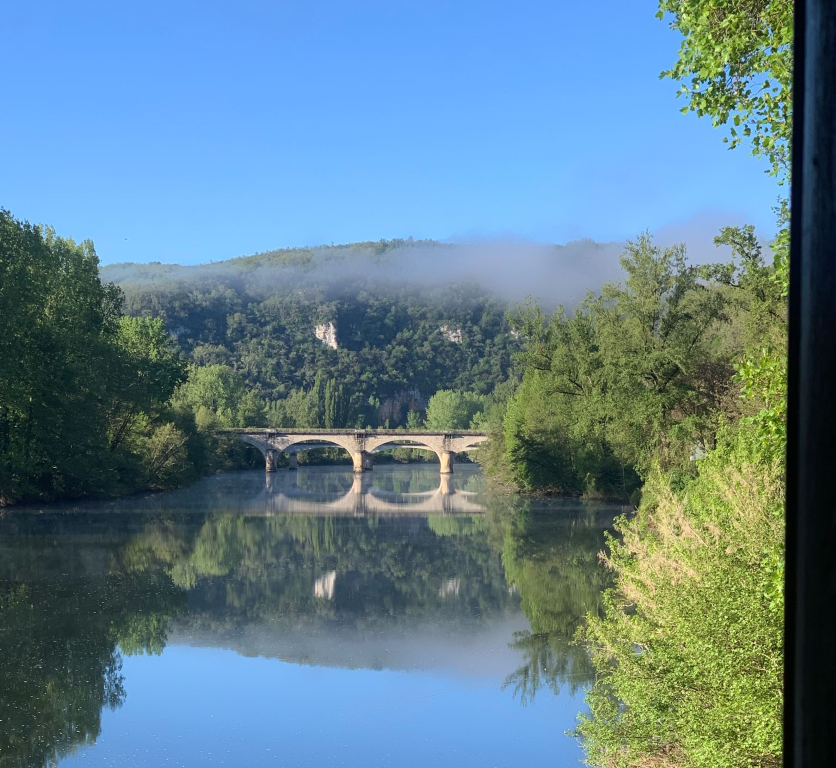 view from the kitchen of a blue river and a distant stone bridge, and a hill bejewelled with morning mist in the background