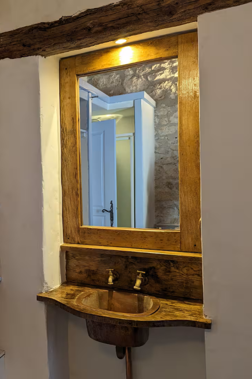 mirror with wooden frame set in the wall above a copper sink held in an appealing curved wooden surround