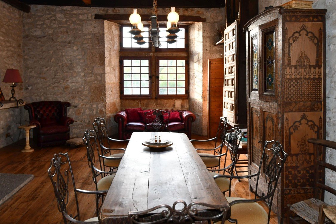 Large dining table, wooden rafters, with a river view beyond. The sun is shining through the window onto a wooden floor.