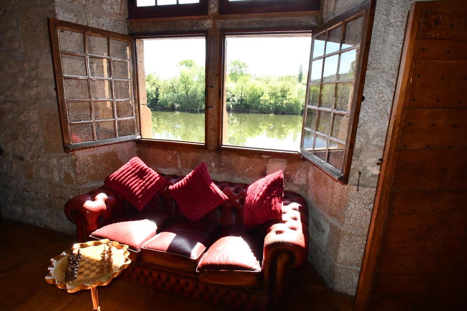 large mullioned windows overlooking a river, viewed from inside a room containing a large leather sofa